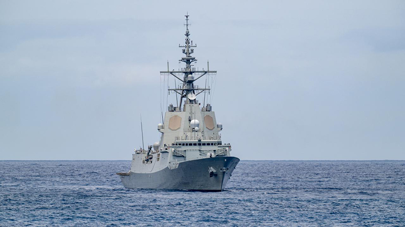 A naval vessel sails through a flat expanse of ocean.